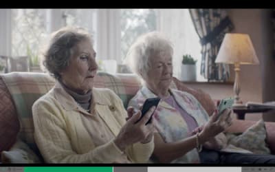 two older women sitting on a couch looking at a cell phone
