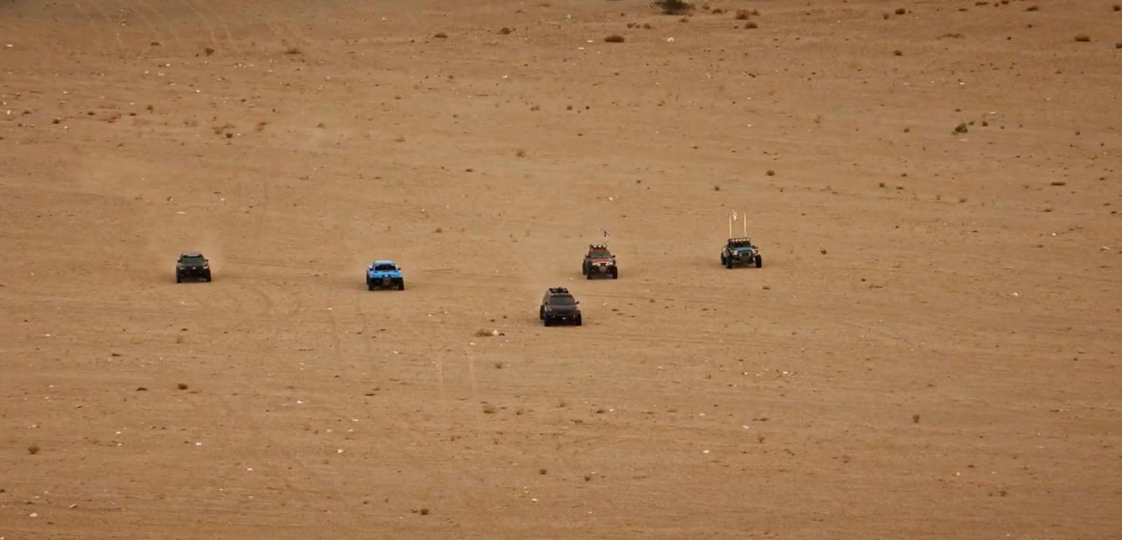a group of four cars driving across a sandy field