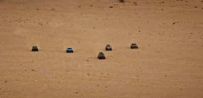 a group of four cars driving across a sandy field