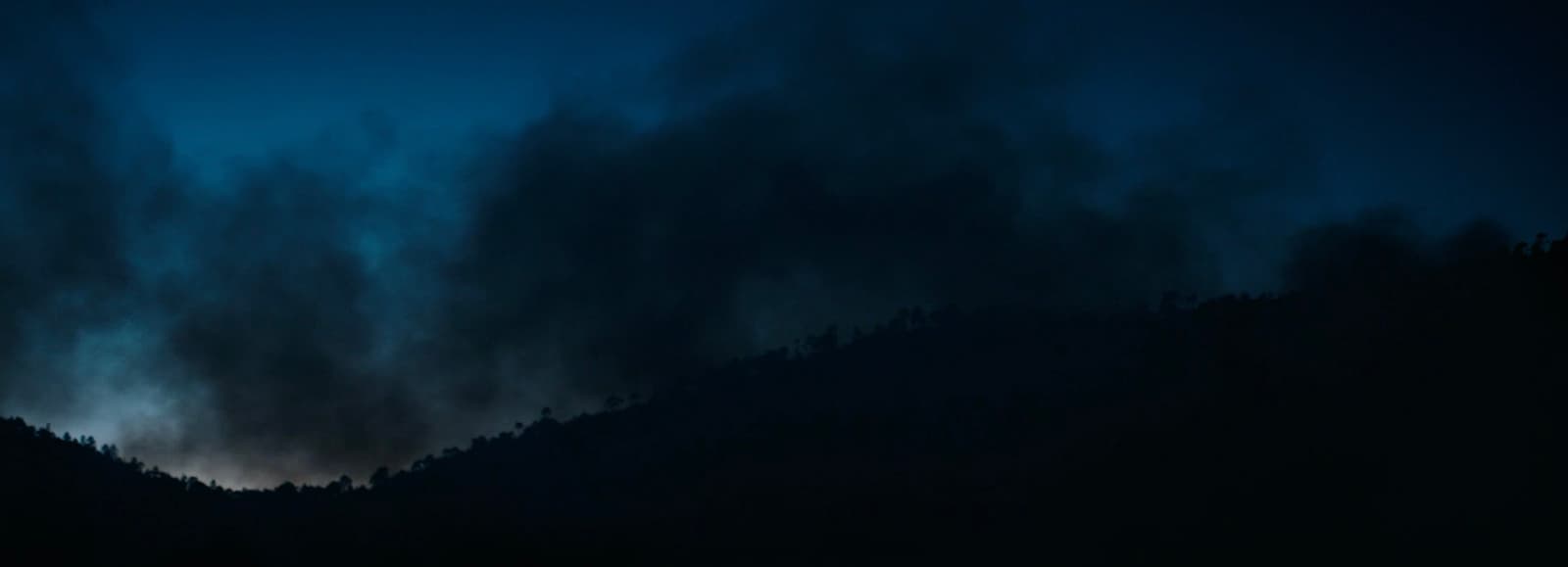 a dark sky with clouds and trees in the foreground