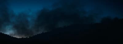 a dark sky with clouds and trees in the foreground