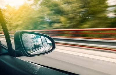 a car's side view mirror with trees in the background