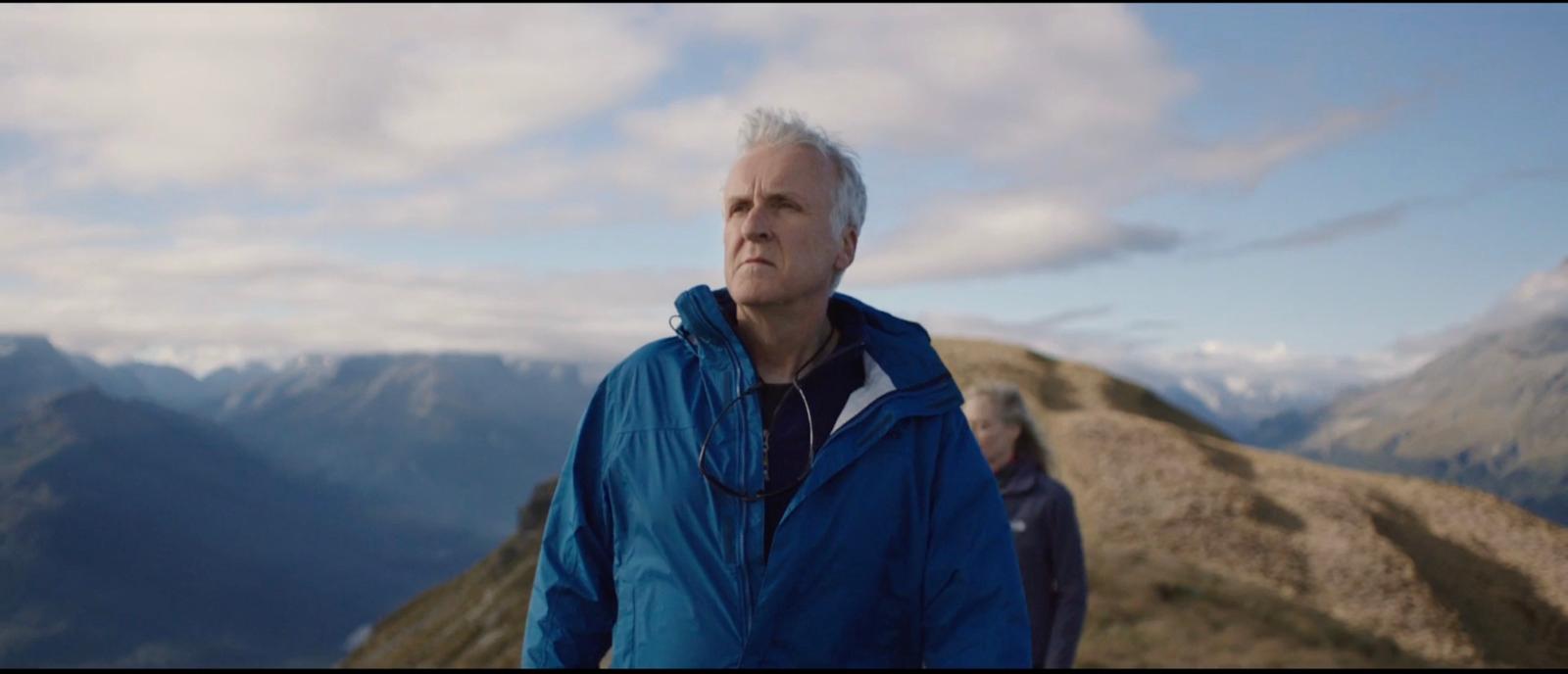 a man in a blue jacket standing on top of a mountain