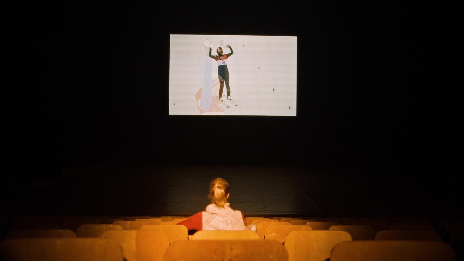 a little girl sitting in a chair in front of a screen