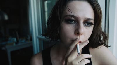 a woman smoking a cigarette in front of a window