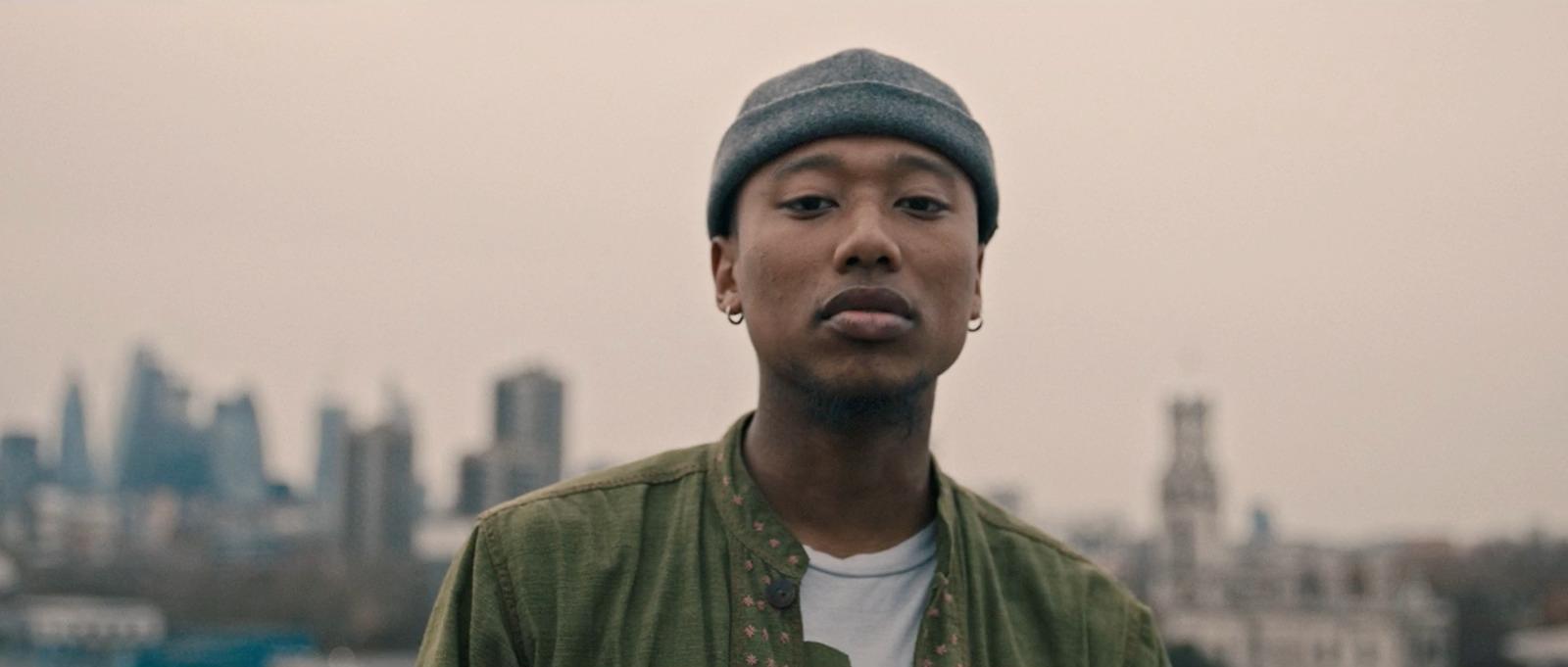 a man in a green jacket with a city in the background