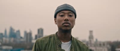 a man in a green jacket with a city in the background