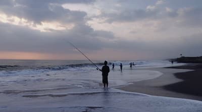 a man standing on top of a beach holding a fishing pole