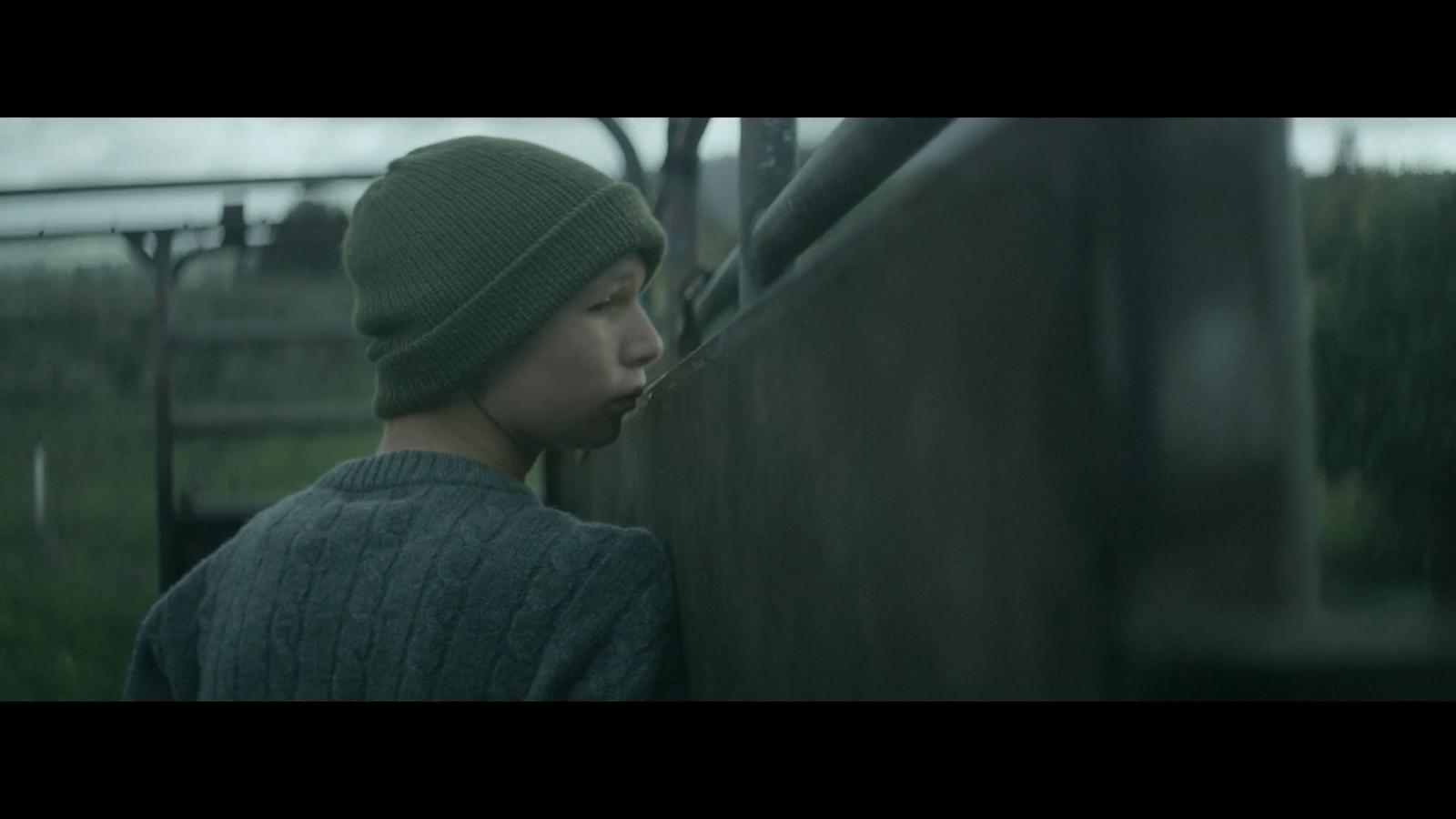 a young man wearing a green hat standing next to a fence