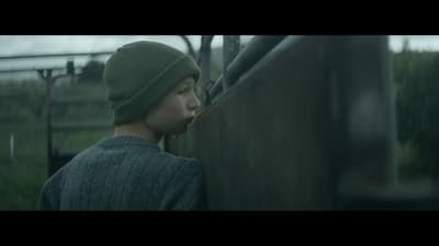 a young man wearing a green hat standing next to a fence