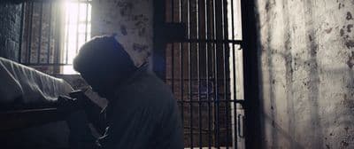 a man sitting in a jail cell holding a cell phone