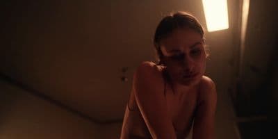 a naked woman sitting on a bed in a dimly lit room