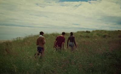 three young men are walking through tall grass