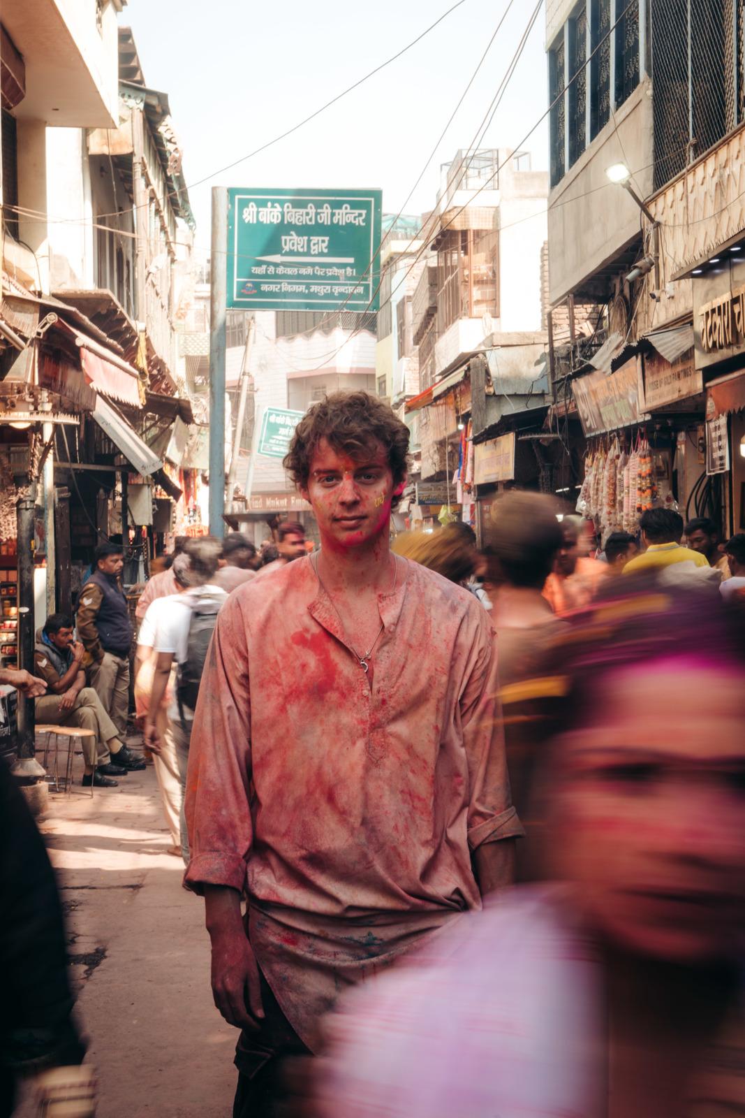 a man with red paint on his face walking down a crowded street