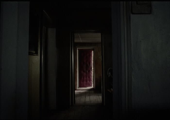 a dark hallway with a red door and a red curtain