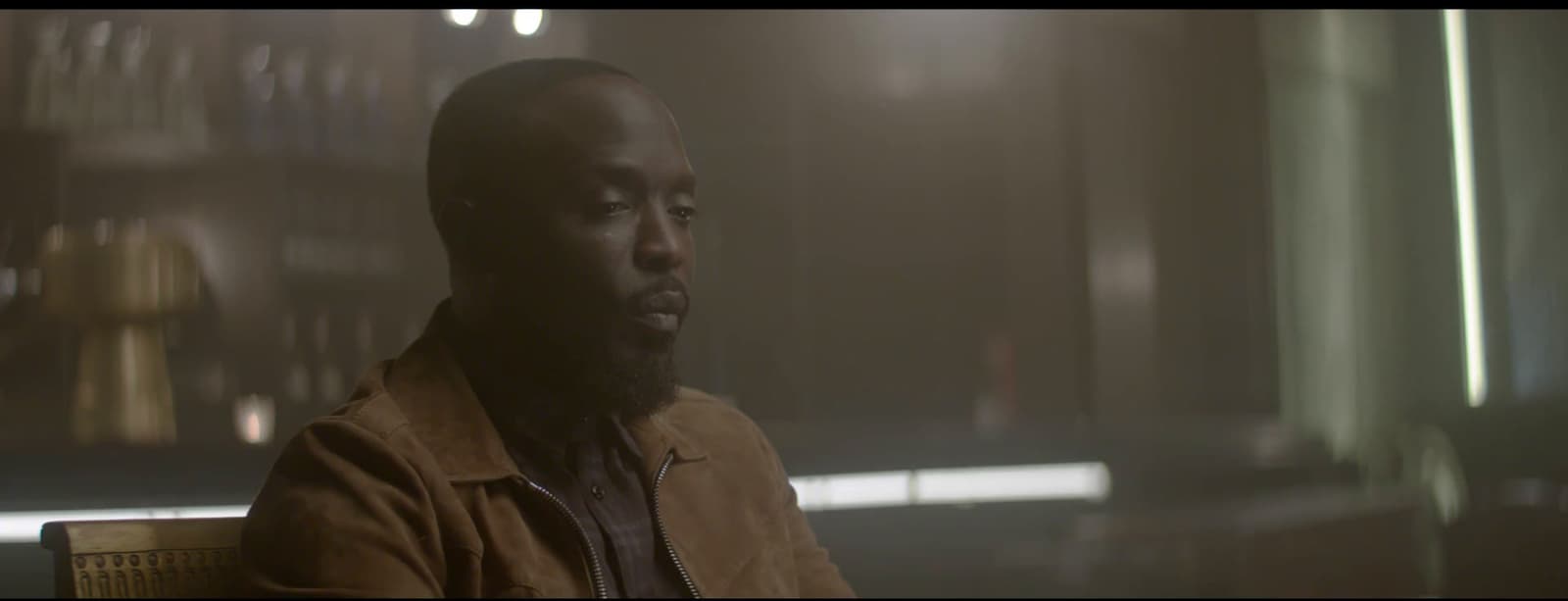 a man in a brown jacket sitting in a room