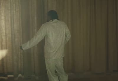 a man in a white suit standing in front of a curtain