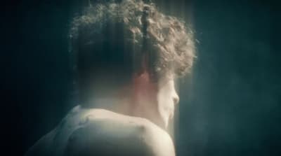 a man with curly hair standing in front of a window
