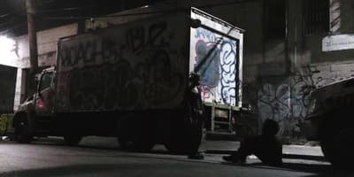a man sitting on the side of a road next to a truck