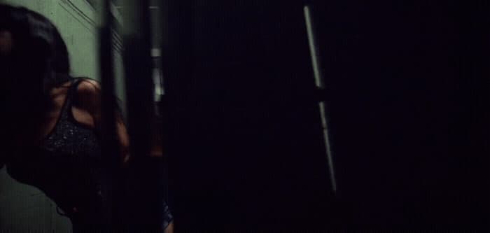 a woman standing in a dark room next to a wall