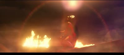 a woman in a red dress standing in front of a fire