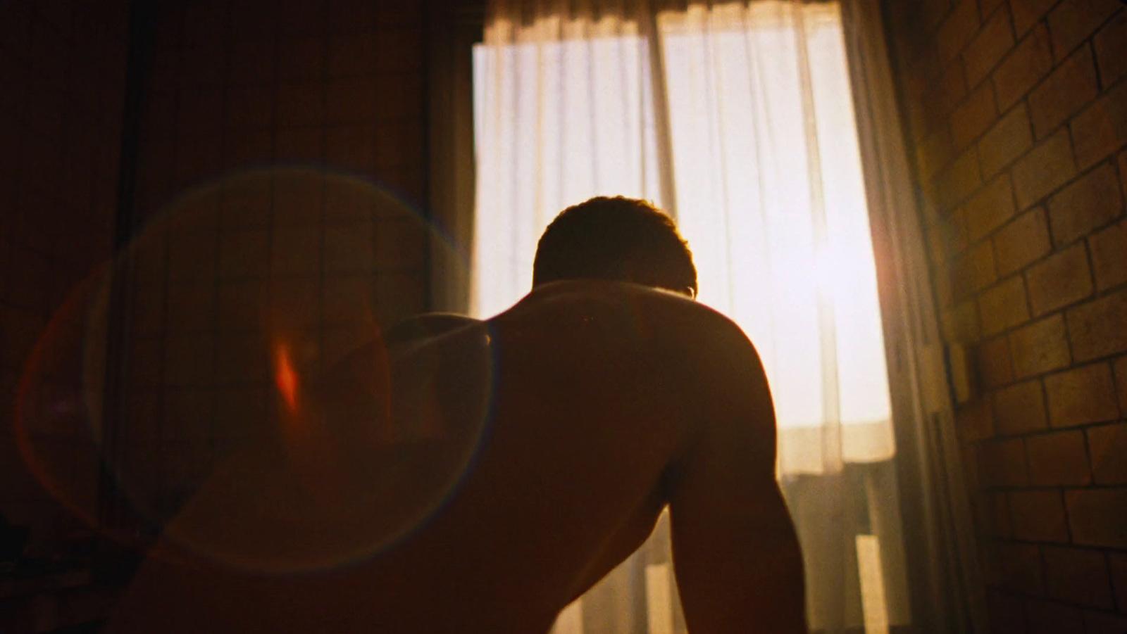a shirtless man standing in front of a window