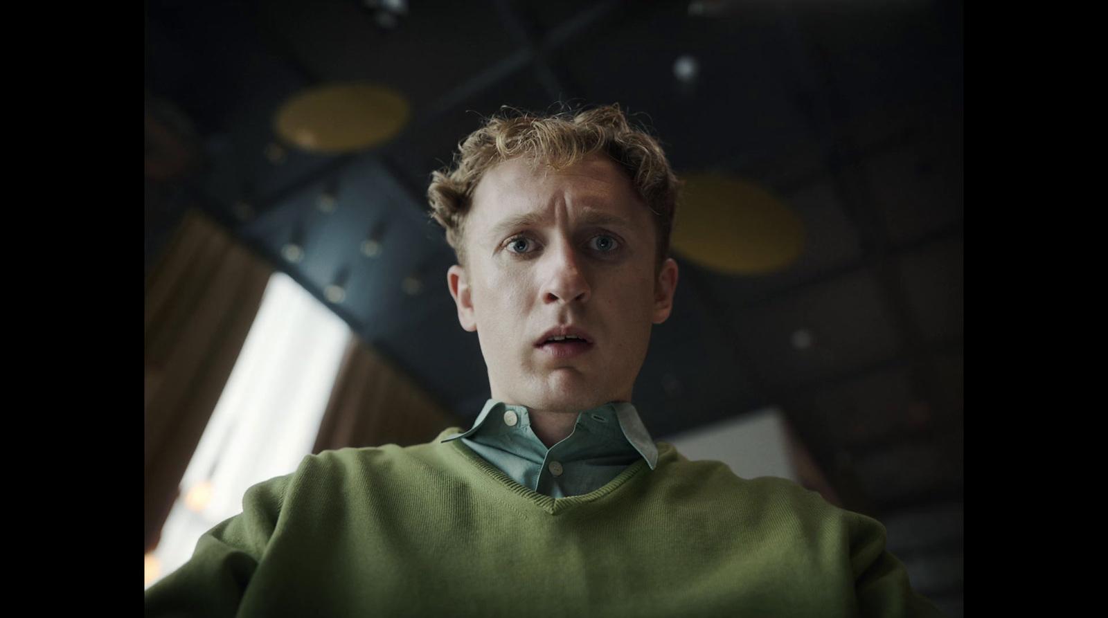 a young man in a green sweater looking at the camera