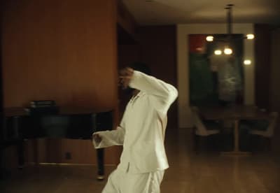 a man in a white suit standing in front of a piano