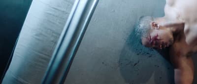 a shirtless man laying in a shower stall