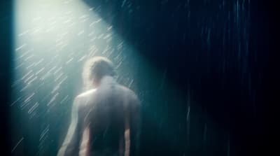 a man standing in the rain under a bright light