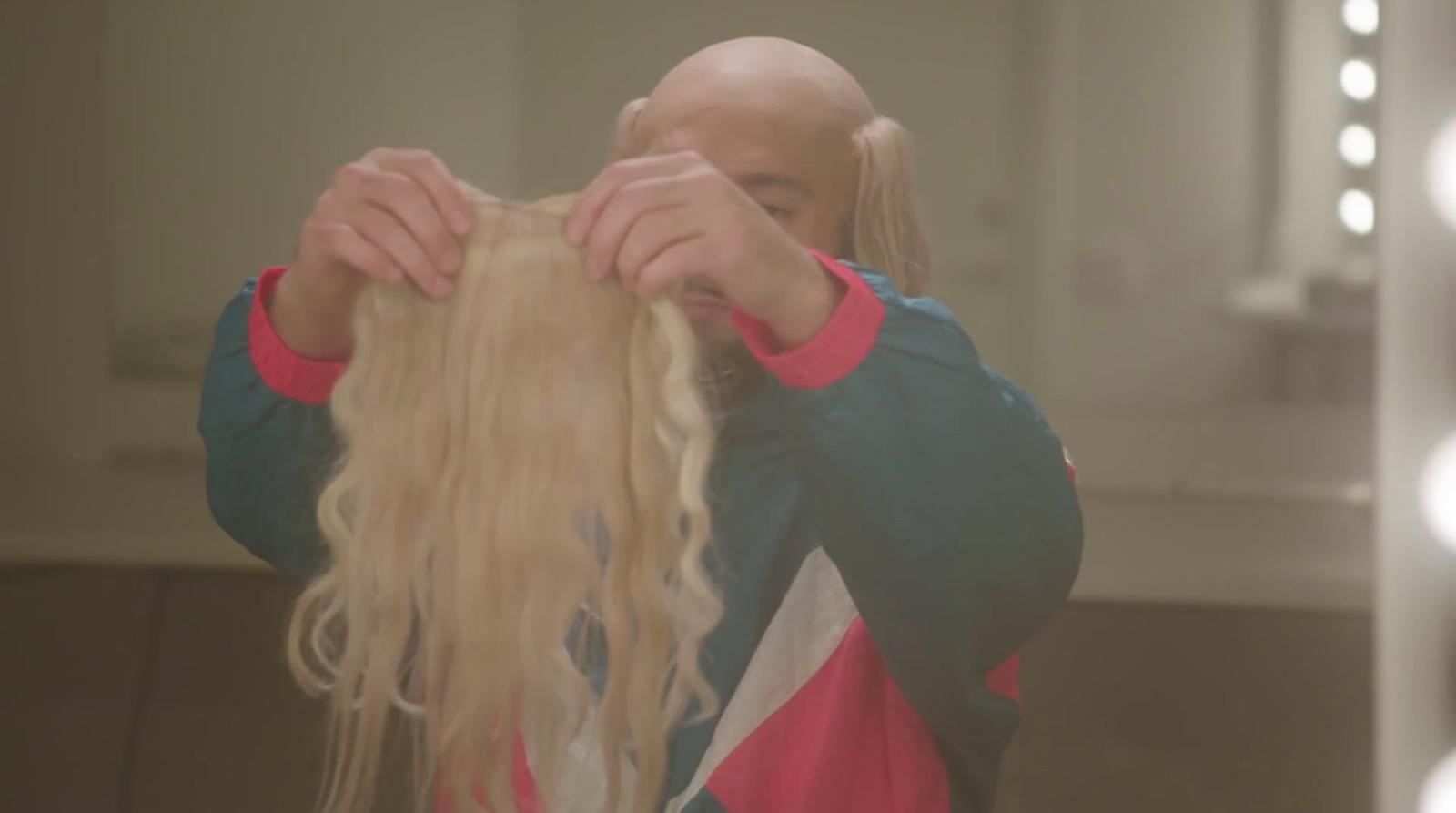 a man with long blonde hair standing in front of a mirror