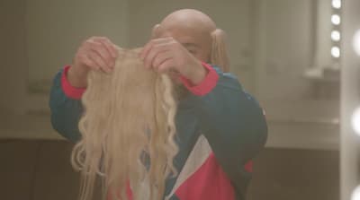 a man with long blonde hair standing in front of a mirror