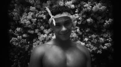 a shirtless man standing in front of a bush
