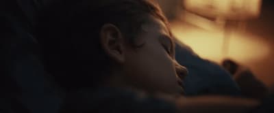 a young boy sleeping on a bed next to a lamp