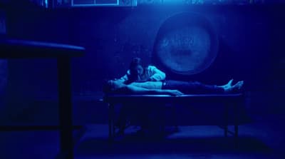 a man and a woman laying on a table in a dark room