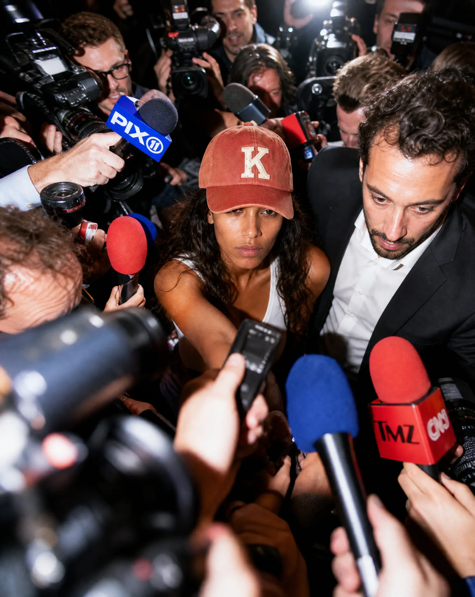 AI-generated editorial shot of a model in the K baseball cap surrounded by paparazzi and microphones