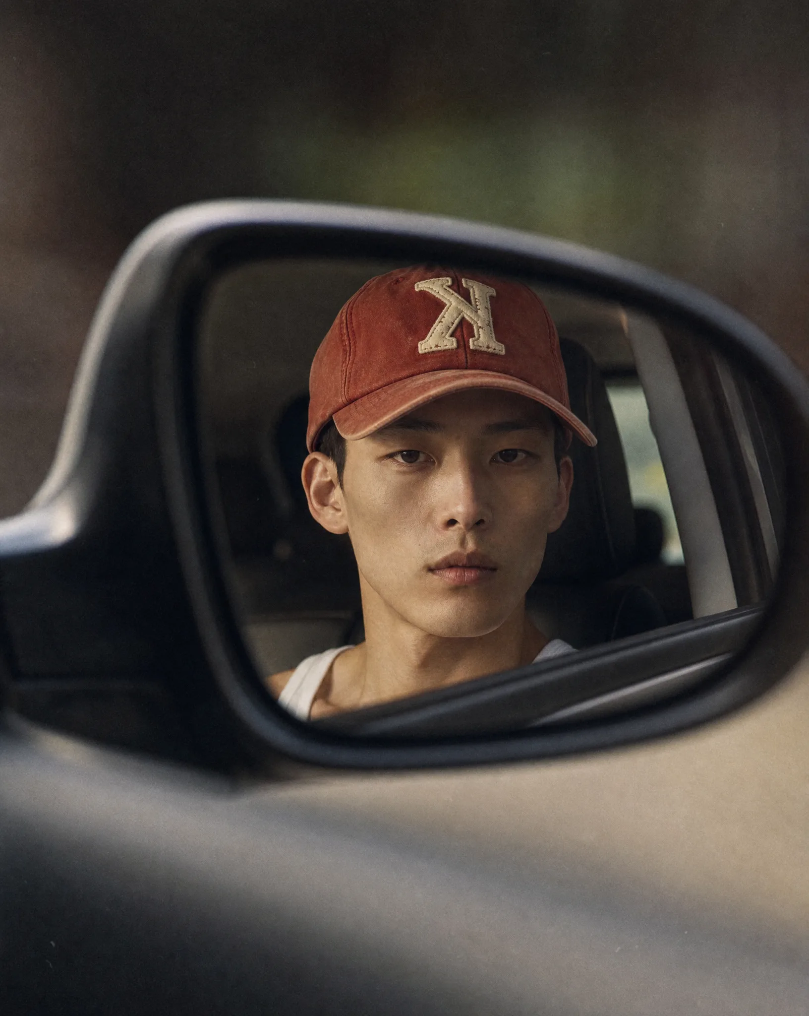 AI-generated editorial shot of a model wearing the K baseball cap reflected in a car side mirror